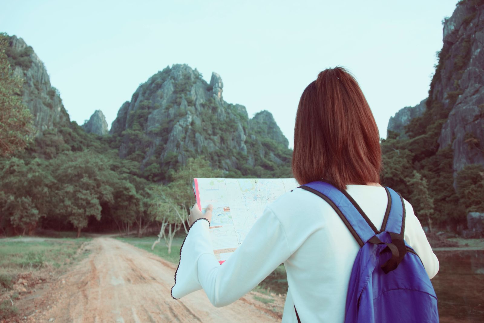 Une voyageuse au sac à dos violet consulte une carte avant de poursuivre sur un sentier parmi des montagnes verdoyantes