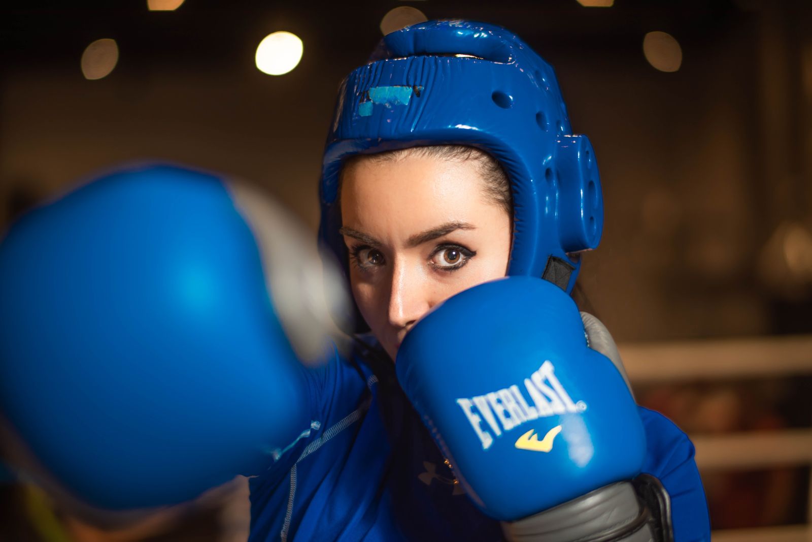 Eine Boxerin mit blauem Kopfschutz und Handschuhen blickt nach vorn, während sie einen Schlag ausführt