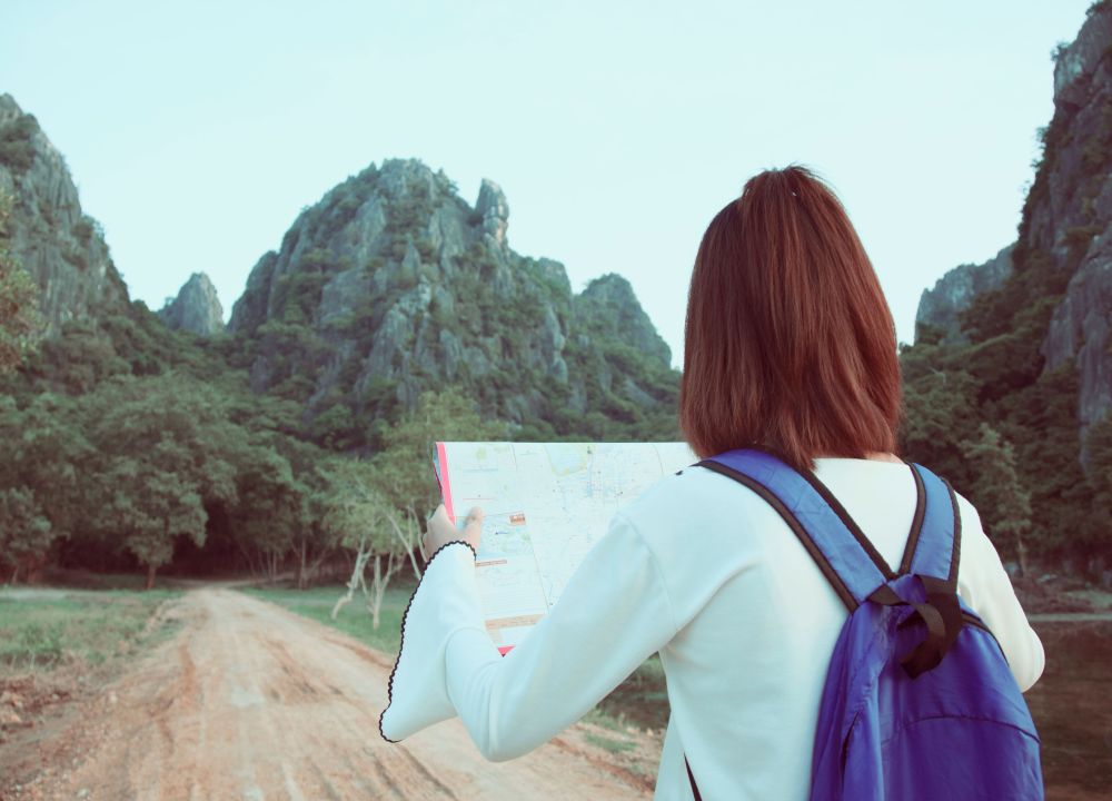A traveller with a purple backpack consults a map before continuing along a path among green mountains