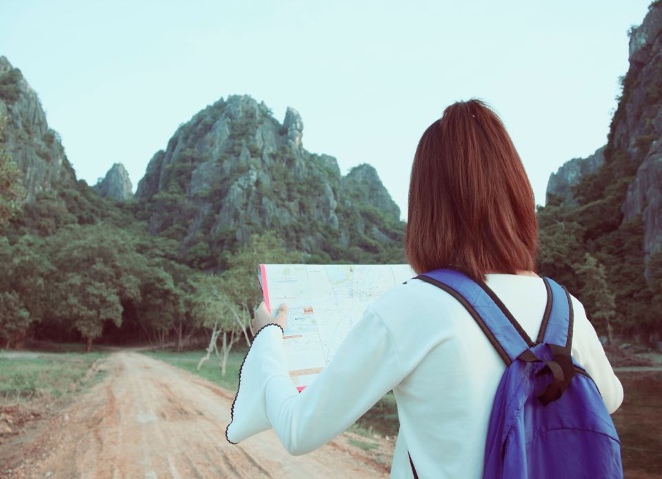 Una viaggiatrice con zaino viola consulta una mappa prima di proseguire lungo un sentiero tra montagne verdi